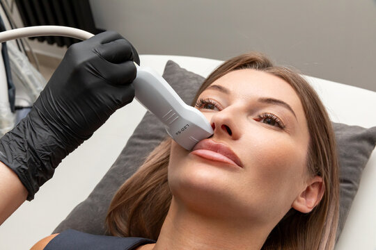 Removal of filler from lips in cosmetology clinic with ultrasound examination. Female patient receiving facial treatment. Diagnostics of internal organs, superficial structures and peripheral vessels