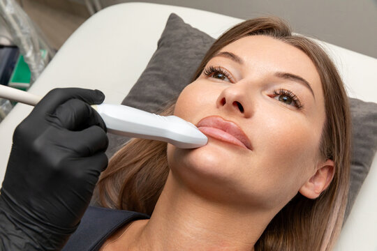 Removal of filler from lips in cosmetology clinic with ultrasound examination. Female patient receiving facial treatment. Diagnostics of internal organs, superficial structures and peripheral vessels