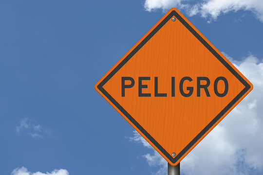 Orange Danger Peligro Spanish warning sign with sky for risk prevention