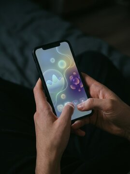 Man holding smartphone with colorful abstract wallpaper on screen. Male hands using mobile phone in dark room. Digital technology, mobile app and modern gadget usage concept.