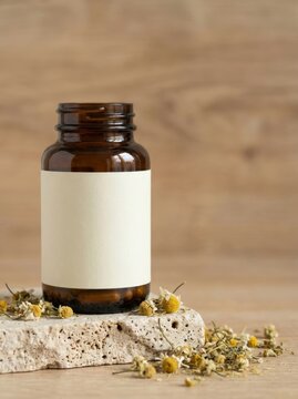 Amber glass bottle with blank label on stone podium with dried chamomile flowers on wooden background. Natural herbal supplement and apothecary product mockup.