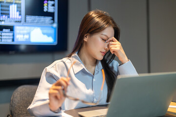 Asian female employee holding glasses suffering from computer vision syndrome and eye fatigue at...