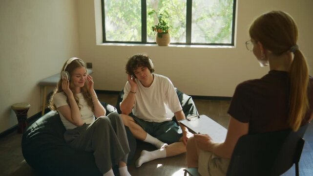 Two people sit on the floor in a psychology session while wearing headphones, listening to therapy music with a therapist across from them