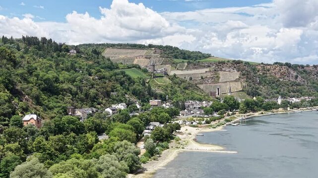 Aerial view of the Rhine River near Bacharach, Germany, with hillside vineyards, traditional houses and historic architecture surrounded by green landscape in the Upper Middle Rhine Valley.