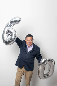 60-year-old Latino man with a dark skin displays 60 shaped balloons to celebrate his birthday and his entry into his old age