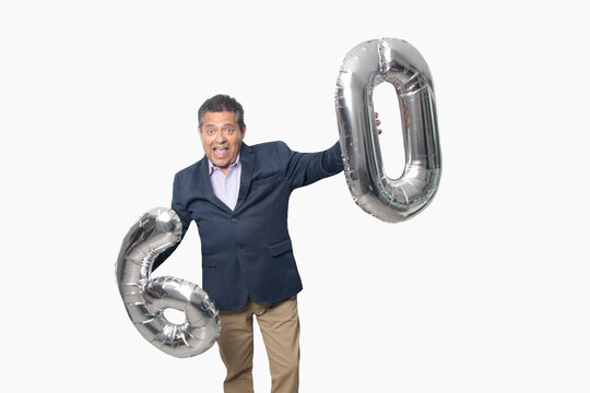 60-year-old Latino man with a dark skin displays 60 shaped balloons to celebrate his birthday and his entry into his old age