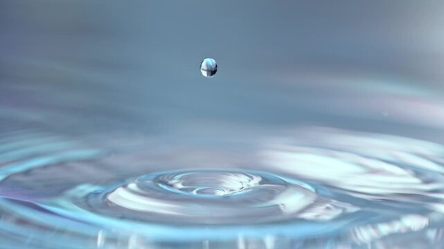 Super Slow Motion Shot of Water Drop Falling into Light Blue Water Surface at 1000fps.