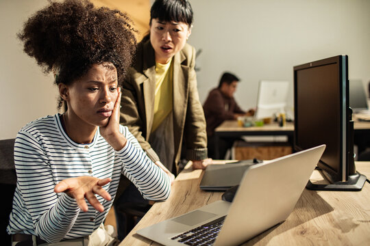 Two coworkers troubleshooting a laptop problem in a modern office