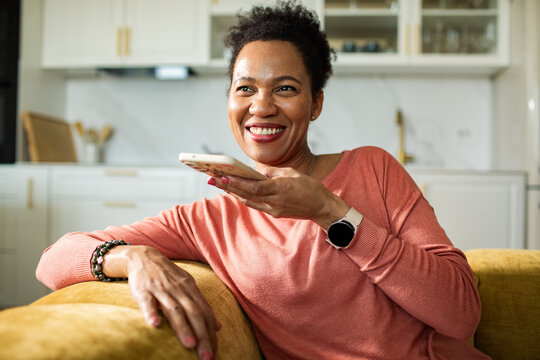 Smiling woman using smartphone voice assistant in home kitchen