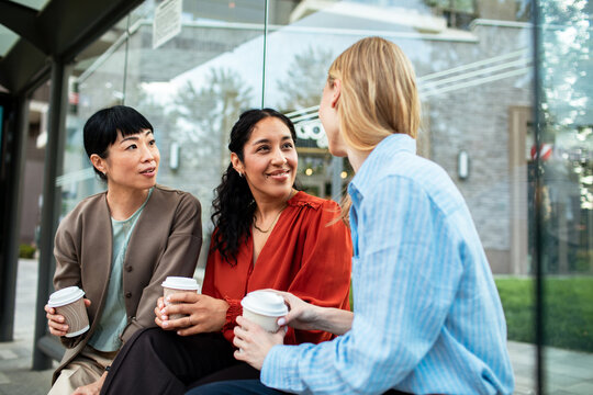 Three coworkers chatting over coffee at city bus stop