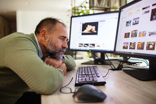 Bearded middle-aged man bored at dual computer monitors in home office
