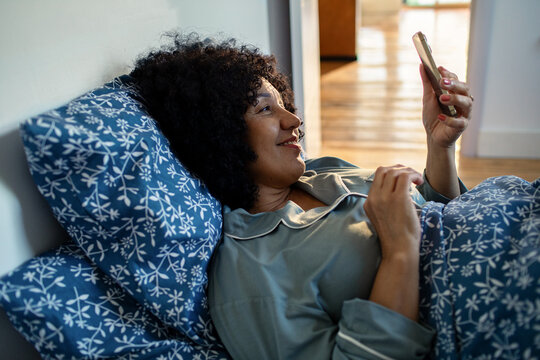 Smiling woman texting on smartphone in bed at home