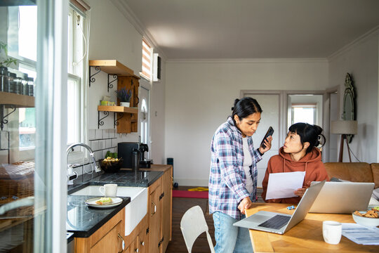 Two women managing household bills with laptop and phone at home