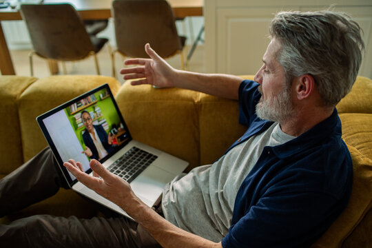 Mature man on sofa having video call on laptop at home