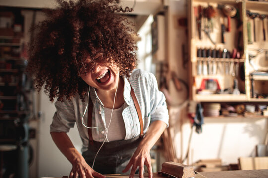 Woman carpenter laughing while sanding wood in workshop
