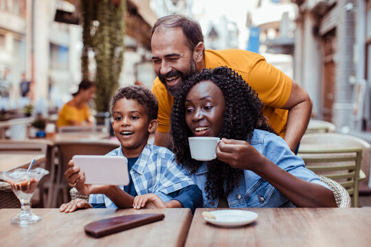 Happy family watching smartphone at outdoor cafe in city
