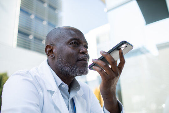 Mature male doctor speaking into smartphone outside hospital