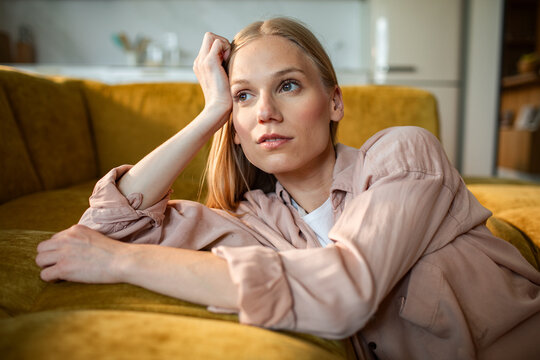 Thoughtful young woman resting on sofa at home