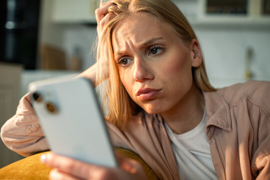 Worried young woman checking phone at home