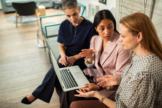Three businesswomen discussing strategy on laptop in modern office