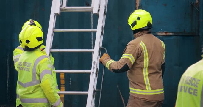 Firefighter crew &ndash; emergency service fireman rescue in action. In uniform in response to fire with firefighting ladder against building.