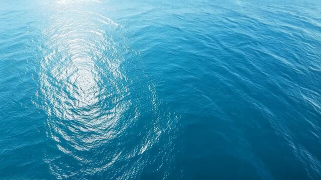 Aerial view of calm blue ocean with sun glare creating rippling light patterns on the water surface