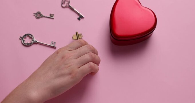 Woman choosing key to heart shaped box on pink background, closeup