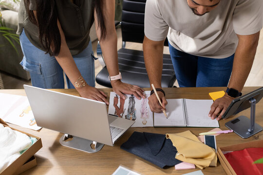African American designers leaning over wooden worktable, sketching with pencil and fabric swatches