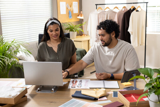 African American designers sitting at studio reviewing laptop and swatches with printed sketches