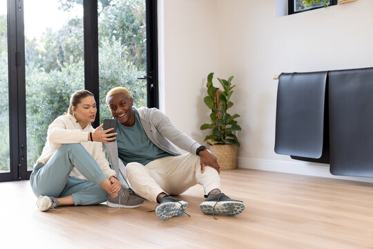 African American couple sitting on wood floor by glass doors holding smartphone and wearing shoes