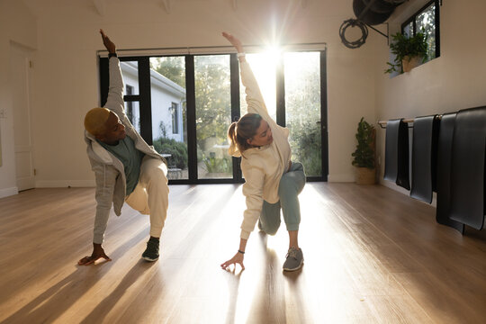 African friends lunging in studio in sportswear on wood floor by glass doors, wrist tracker
