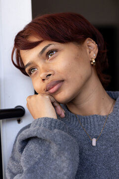 Adult woman leaning at home doorway, resting chin on hand and gazing upward, wearing gray sweater