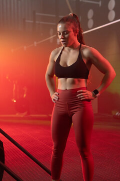 Female athlete standing and resting in gym wearing black sports bra red leggings near training tire