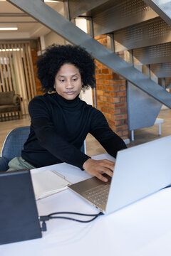 African American man working on silver laptop at desk wearing black turtleneck with notebook hub