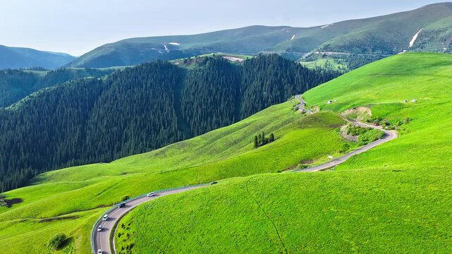 Aerial view of cars driving on a winding mountain pass road surrounded by green slopes on Duku Highway, Xinjiang, China.