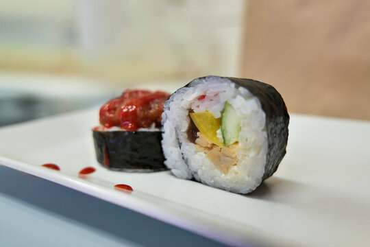 Two pieces of large futomaki rolls with vegetable filling and a gunkan sushi topped with finely chopped fish on a light rectangular plate. Japanese sushi assortment concept