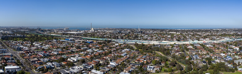 Obraz premium Panoramic aerial view of &nbsp;the residential rooftops of Yarraville and Spotswood, tracing the M1 West Gate Freeway and industrial coastline toward Port Phillip Bay. Melbourne, Victoria, Australia