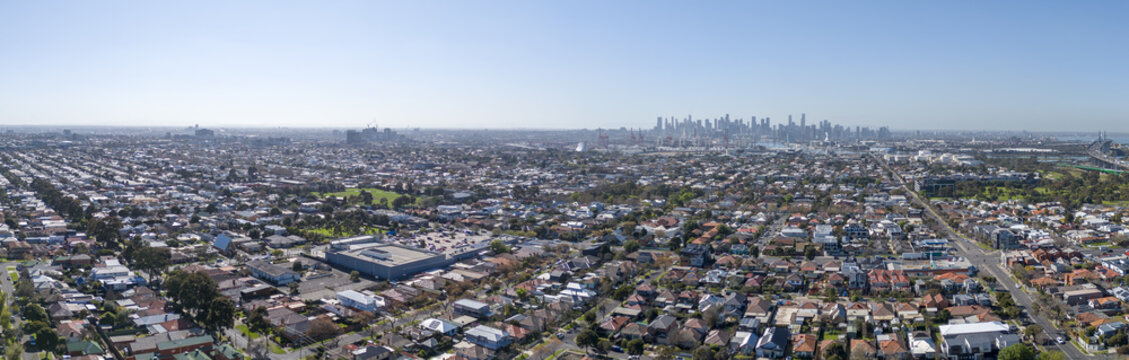 Wide panoramic aerial view sweeping over the suburban residential grid of Yarraville and the inner west, looking east toward the distant city skyline. Melbourne, Victoria, Australia