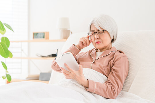 読書中に目の疲れを感じるシニア女性。老眼や眼精疲労に悩む様子