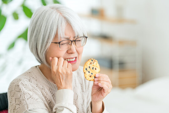 硬いせんべいを食べて歯の痛みに悩むシニア女性。噛みにくさを感じる高齢者