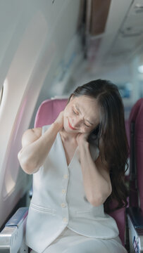 Asian woman passenger suffering from neck pain while sitting in airplane seat during long flight