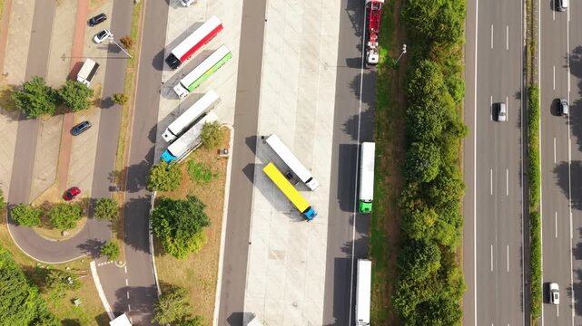 Aerial perspective of trucks parked in a loading zone adjacent to a highway, highlighting the orderly layout and nearby vegetation