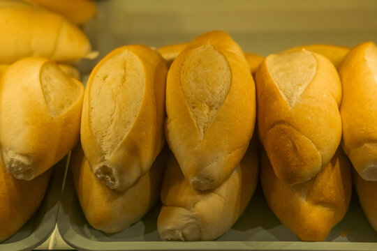 Close-up of baked bread rolls with a lengthwise cut stacked in a plastic tray behind a display glass.