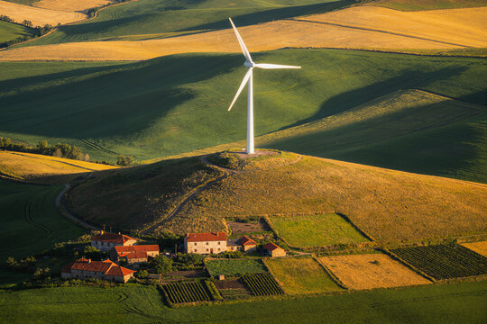 Wind turbine above farmstead and patchwork fields, aerial view