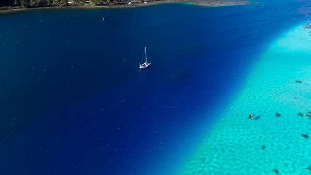 Lone sailboat surrounded by vast blue and turquoise tropical ocean