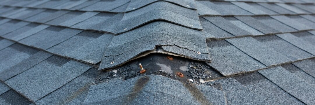Damaged grey asphalt shingles on a rooftop showing signs of wear and tear with curling and lifting edges creating need for repair.