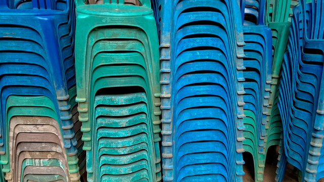 Front view close up of multiple blue, green, and brown plastic chairs stacked neatly in vertical columns in a storage space or event rental shop.