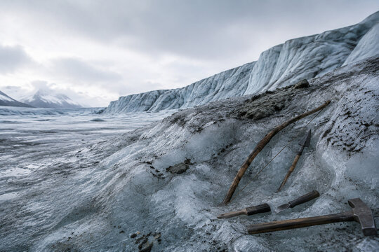 Glacier landscape with small excavation site, ancient bow and arrowhead in ice, archaeological tools