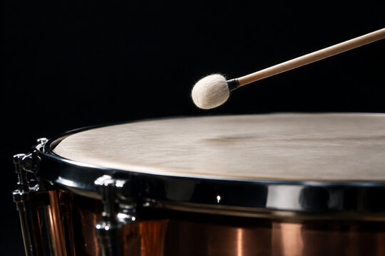 Drumstick poised just above the skin of a timpani drum.