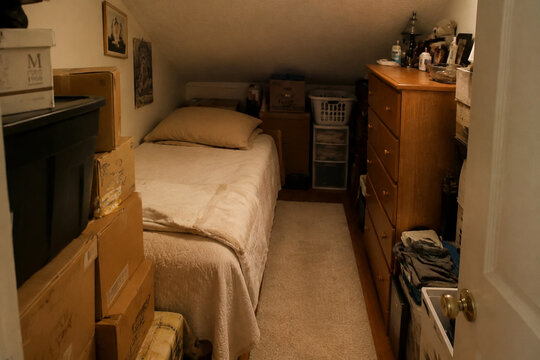 Narrow bed in cramped room with stacked boxes and dresser, small living space and storage concept
